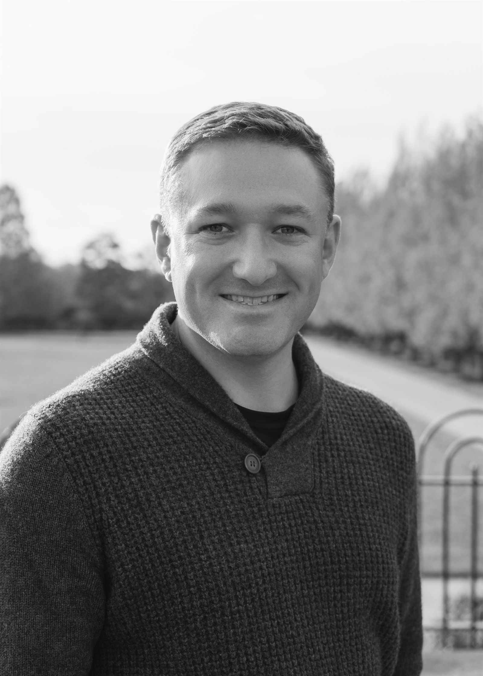 Black-and-white portrait of Max Triantos smiling outdoors in a dark sweater.